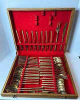 Top view of the box open showing the full assortment of gold-toned cutlery neatly organized in red velvet slots.