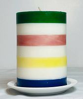 Front view of the Hudson’s Bay multi-striped pillar candle on a white ceramic dish showing green, white, red, white, yellow, and blue stripes.