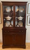 Knetchel mahogany hutch from front showing glass door upper cabinet with decorative china inside and closed lower storage with drawer and doors.