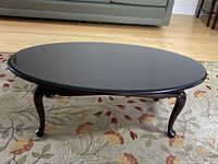 Front view of the oval coffee table with glass top placed on patterned rug