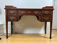 Front view of mahogany writing desk showing overall structure, five drawers and brass pull handles.