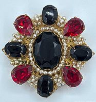 Top view of brooch showing red and black gems with seed pearls and ornate gold-tone setting.