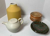 Four items together: yellow vase, white teapot, round lidded pottery container, and green ashtray.