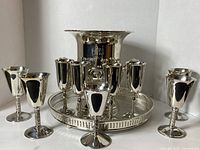 Front view of the silver plated ice bucket, tray, flutes and goblets showing the full set arranged with ice bucket centered on gallery tray surrounded by glasses