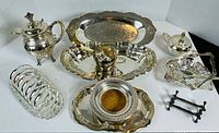 Full view of all silver-plate items arranged on white background showing trays, pot, sugar and creamer, napkin holder, baskets, and napkin rings.