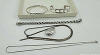 Overview of all pieces on tray: twisted bangle, cuff-style bracelet, thick chain bracelet, two chains with locket and plain chain