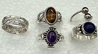 Five sterling silver rings displayed, showing varied designs and semi-precious stones with some wear.