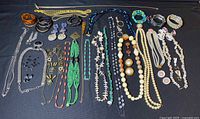 Full display of vintage costume jewelry laid out on black background showing various necklaces, earrings, bracelets, and brooches.