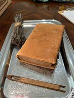 Antique leather book, thread bundle, and wooden shuttle on ornate silver tray.