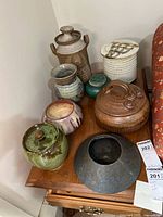 Collection of eight artisan pottery jars arranged on wood table, variety of shapes and glazed colors, some with lids.