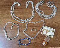 Full display of all jewelry items including crystal necklaces, bracelet, earrings, and cameo pins on wood surface.
