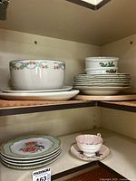 Wide view of shelves showing a variety of porcelain bowls, plates and tea cups and saucers with floral designs.
