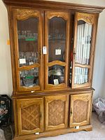 Front view of china hutch showing three glass doors with shelving inside, three wooden cabinet doors below, carved decorative details on upper edges and door frames.