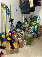 View of brooms, paper towels, spray bottles, and cleaning products stacked in a corner on the floor.