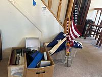 Overall photo of the lot showing boxes in cardboard containers and three American flags in a glass jar