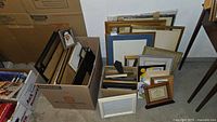 Photo showing a large collection of assorted picture frames packed in boxes and leaning against a wall.