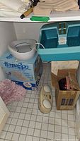 View of the Home Spa foot bath unit in teal blue next to a white plastic bed pan, vintage Dr. Schools foot massager, and a box containing an infrared heat lamp.