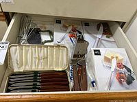 Photo from drawer showing Mikasa butter knives in original packaging along with whisks and chopper