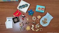 Overview of lot: various pins and brooches including coin medallion pins in white box, enamel maple leaf pins in turquoise box, red pouch, embroidered brooch, enamel and gold-tone pieces