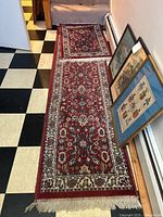 Photo showing the long narrow red floral runner rug laid out on a black and white checkered floor beside framed pictures.