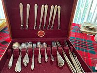 Full view of the silverplate cutlery arranged inside the open wooden box with burgundy velvet lining.