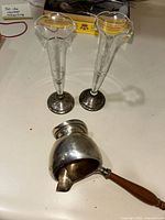 Two sterling silver bud vases with clear glass tops and a sterling silver handled sauce bowl with wooden handle, all placed on table surface
