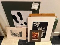 Multiple unframed prints and artworks stacked together, showing a mix of architectural, abstract, and photographic images
