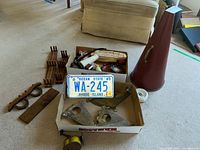 Overview of various vintage and antique items including license plate in box, wall hooks, eyeglasses, and other small items on floor