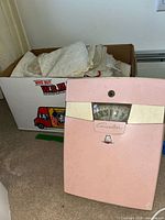 Box of folded vintage linens next to pink Counselor scale on floor.