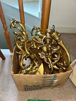 Photo of multiple gold-tone ornate wall sconces packed inside a box showing detailed scroll and floral designs.