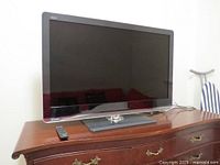 Front view of the 49-inch Sharp TV placed on wooden furniture with remote on the surface.