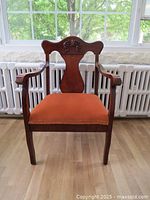 Full front view of the antique mahogany armchair showing rust orange fabric upholstery and armrests.