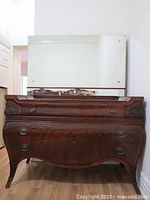 Front view of antique mahogany dresser with ornate mirror and brass handles showing carved details and shape of the dresser.