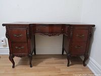 Front view of antique mahogany desk showing ornate wood carvings and five drawers with metal handles.