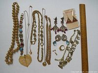 Overview of assorted gold-toned and silver-toned jewelry including necklaces, bracelets, earrings, and ring with a ruler for scale.