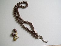 Full view of brown imitation pearl necklace and matching dangle earrings on white background