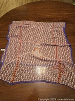 Full view of scarf laid out flat on a wooden surface showing the overall logo print design with purple edging and accent motifs.