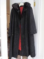 Black Persian lamb fur coat hanging, showing textured lamb fur material and black fur collar.