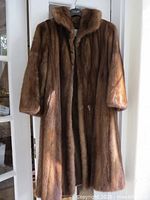 Front view of the Eaton light brown mink fur coat hanging on a hanger in natural light.