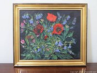 Full view of framed floral oil painting showing vibrant red poppies and bluebell flowers on dark background.