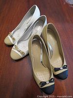 Two pairs of Geox women's dress pumps placed on wooden surface, white/beige pair and beige/brown pair with black accents.
