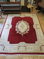 Top view of red-centered rug with ivory border laid on hardwood floor, showing central medallion