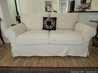 Front view of beige/cream IKEA sofa with floral embroidered decorative pillow on two-seat seating.