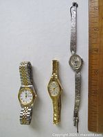 Photo showing three ladies wristwatches arranged with a ruler for size reference, highlighting different gold-tone and silver-tone metal bracelets and various dial shapes and designs.