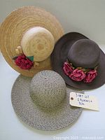 Three wide-brim hats laid flat showing overall shapes and floral details on beige and brown hats, black and white patterned hat included.