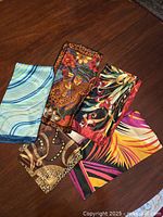 Lot of 5 scarves laid out on table showing various patterns and colors.