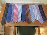 Photo showing 12 men's silk neckties arranged side by side on a wooden table, displaying various patterns and colors including stripes, polka dots, plaid, and solids.