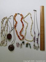 Full lot laid out with ruler for scale, showing 5 necklaces and 8 charms/pendants of mixed stones including agate, jade, quartz, and other materials.