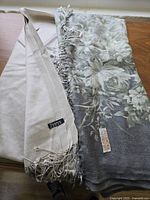 Photo showing the scarf folded with visible floral pattern, solid beige area, and tassel fringe edges.
