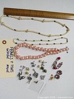 Full view of all items showing three necklaces arranged horizontally with assorted earrings beneath. Includes ruler for scale showing size.